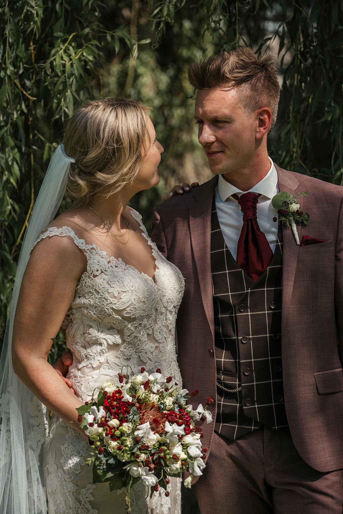 men wearing brown suit blazer  plaid waistcoat  red ascot tie   and a girl wearing a wedding dress